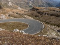 a curve in the mountain road, with two motorcycles on the side of it and mountains and fields in the background