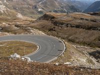 a curve in the mountain road, with two motorcycles on the side of it and mountains and fields in the background