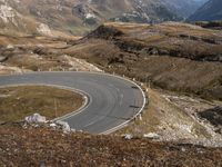 a curve in the mountain road, with two motorcycles on the side of it and mountains and fields in the background