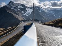 a person on a bicycle riding a road with snow covered mountains in the distance with cars on the side of it