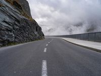 a road in a narrow and dangerous area surrounded by cliffs with fog and mist coming off the rocks