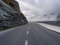 a road in a narrow and dangerous area surrounded by cliffs with fog and mist coming off the rocks