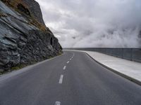 a road in a narrow and dangerous area surrounded by cliffs with fog and mist coming off the rocks