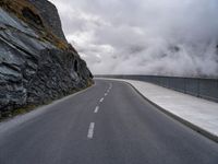 a road in a narrow and dangerous area surrounded by cliffs with fog and mist coming off the rocks