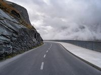 a road in a narrow and dangerous area surrounded by cliffs with fog and mist coming off the rocks