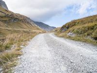 a man rides down a dirt road on an open mountain road in the mountains surrounding a cloudy day