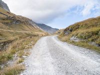 a man rides down a dirt road on an open mountain road in the mountains surrounding a cloudy day