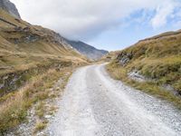 a man rides down a dirt road on an open mountain road in the mountains surrounding a cloudy day