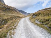 a man rides down a dirt road on an open mountain road in the mountains surrounding a cloudy day