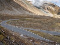 a lone vehicle is going down a mountainous road to pass the mountains behind it,