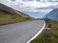 an empty highway stretches along the mountains in switzerland at high altitudes, near a bench next to a road sign