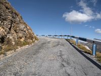 empty road with blue railings near grassy hills and rock side wall, as seen in the distance