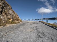 empty road with blue railings near grassy hills and rock side wall, as seen in the distance