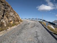 empty road with blue railings near grassy hills and rock side wall, as seen in the distance