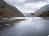 road sign next to empty street, in the mountains, with rain clouds covering the background