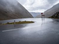 road sign next to empty street, in the mountains, with rain clouds covering the background