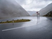 road sign next to empty street, in the mountains, with rain clouds covering the background