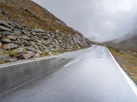 a view from behind of a long mountain road with rocks and stones on the mountains side