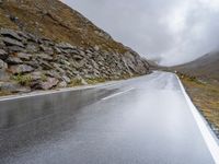 a view from behind of a long mountain road with rocks and stones on the mountains side