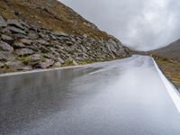 a view from behind of a long mountain road with rocks and stones on the mountains side