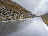 a view from behind of a long mountain road with rocks and stones on the mountains side