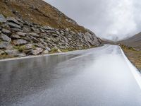 a view from behind of a long mountain road with rocks and stones on the mountains side