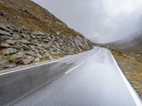 a view from behind of a long mountain road with rocks and stones on the mountains side