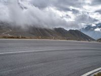 an empty asphalt street with mountains in the distance and a cloudy sky overhead it all