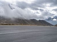 an empty asphalt street with mountains in the distance and a cloudy sky overhead it all