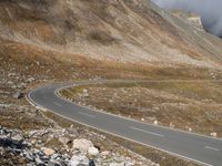 a lone bus driving on the side of a winding road in the mountains, with low clouds