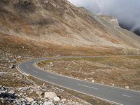 a lone bus driving on the side of a winding road in the mountains, with low clouds