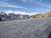 a person is riding a skateboard in the mountains next to a hill slope and snow covered mountains