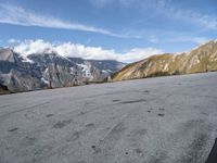 a person is riding a skateboard in the mountains next to a hill slope and snow covered mountains