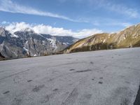 a person is riding a skateboard in the mountains next to a hill slope and snow covered mountains