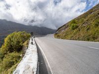 an empty road winds through the mountains below clouds and fogs, with rock walls and vegetation in the foreground