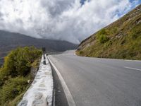 an empty road winds through the mountains below clouds and fogs, with rock walls and vegetation in the foreground