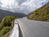 an empty road winds through the mountains below clouds and fogs, with rock walls and vegetation in the foreground