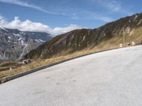 a lone bench is in front of an empty road with mountains in the background with some clouds