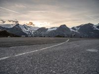 an empty parking lot with snow covered mountains in the background, and vehicles driving beside