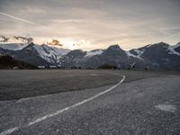 an empty parking lot with snow covered mountains in the background, and vehicles driving beside