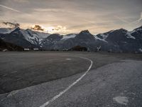 an empty parking lot with snow covered mountains in the background, and vehicles driving beside