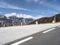 a paved road with snow covered mountains in the distance, with white clouds and blue sky