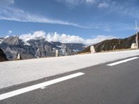 a paved road with snow covered mountains in the distance, with white clouds and blue sky