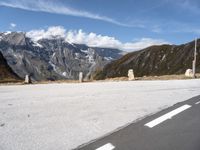 a paved road with snow covered mountains in the distance, with white clouds and blue sky