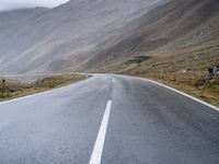 an empty open road leading to mountains with fog above it and a cloudy sky overhead