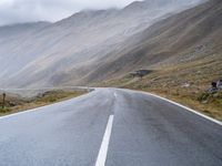 an empty open road leading to mountains with fog above it and a cloudy sky overhead