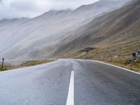 an empty open road leading to mountains with fog above it and a cloudy sky overhead