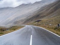 an empty open road leading to mountains with fog above it and a cloudy sky overhead