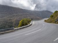 a street lined with trees and hills on either side of a road under a cloudy sky