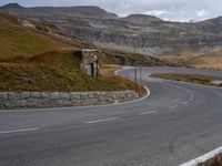 the road has winding curves in it with a stone guardpost on both sides and a rock structure to protect traffic and pedestrians